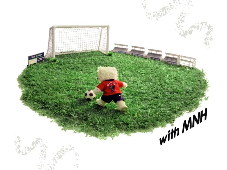 Teddy bear kicking a football on a patch of turf